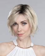 A woman modeling the Ellen Wille Amy Deluxe short bob wig with a side-swept fringe and modern tapered ends.