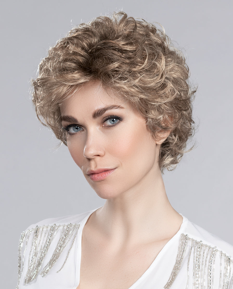 A woman wearing the Ellen Wille City Mono wig, showcasing its texturized shag cut, natural monofilament parting, and invisible extended lace front.