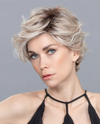 A woman modeling the Ellen Wille Cover Mono Part wig, showcasing its edgy short asymmetrical cut and deep side-swept voluminous styling.