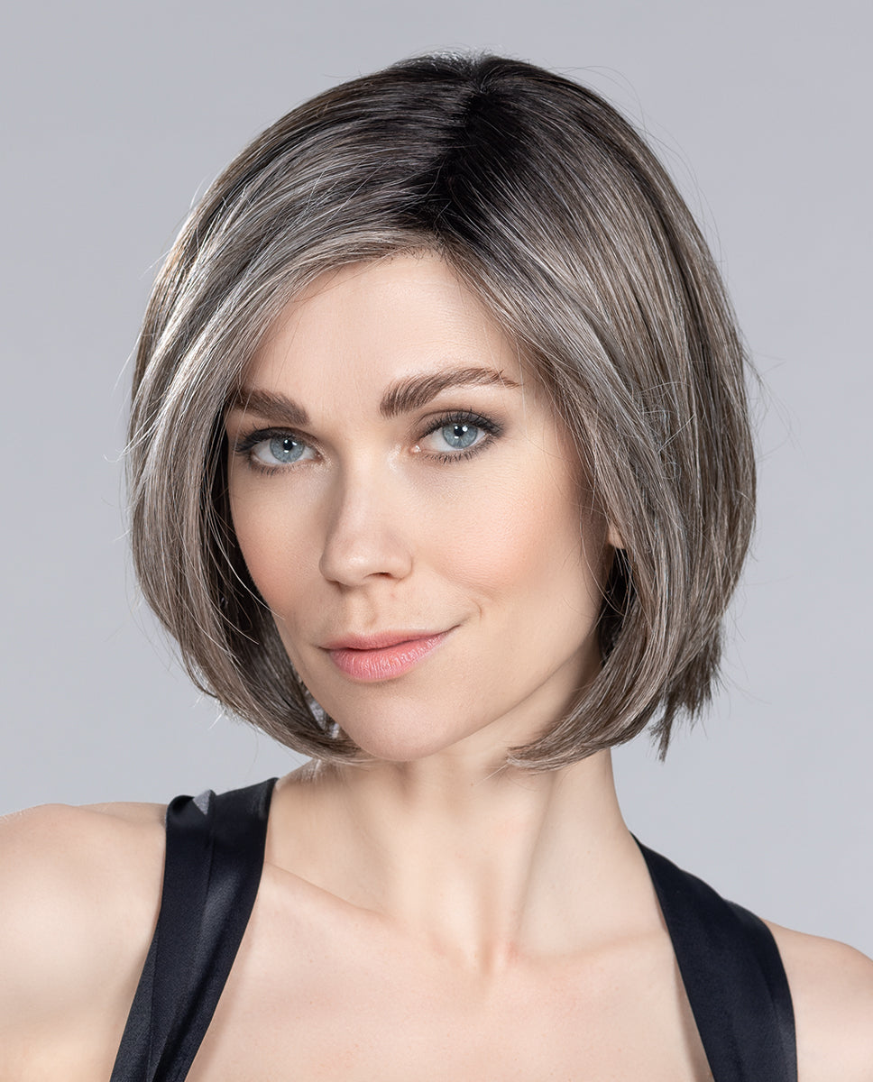 A woman modeling the Ellen Wille Elite Mono Part wig, showcasing its sleek mid-length bob cut and the versatile styling options of its extended lace front.