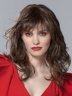 A woman wearing the long Ellen Wille Flash Mono Part synthetic wig, showcasing its messy-chic waves, straight tapered fringe, and natural parting.