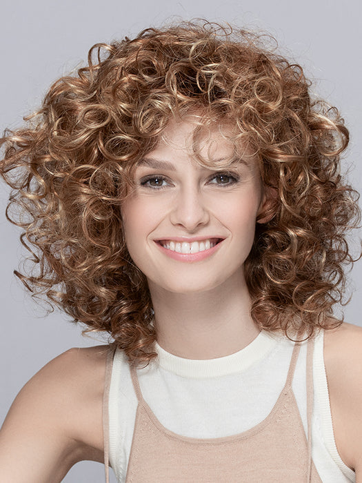 Front view of a woman modeling the Ellen Wille Jamila Plus wig, showcasing its voluminous bouncy curls and natural temple-to-temple lace front hairline.