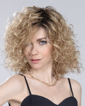 Front view of a woman modeling the Ellen Wille Storyville wig, showcasing its voluminous mid-length cascading curls, soft texture, and natural movement.
